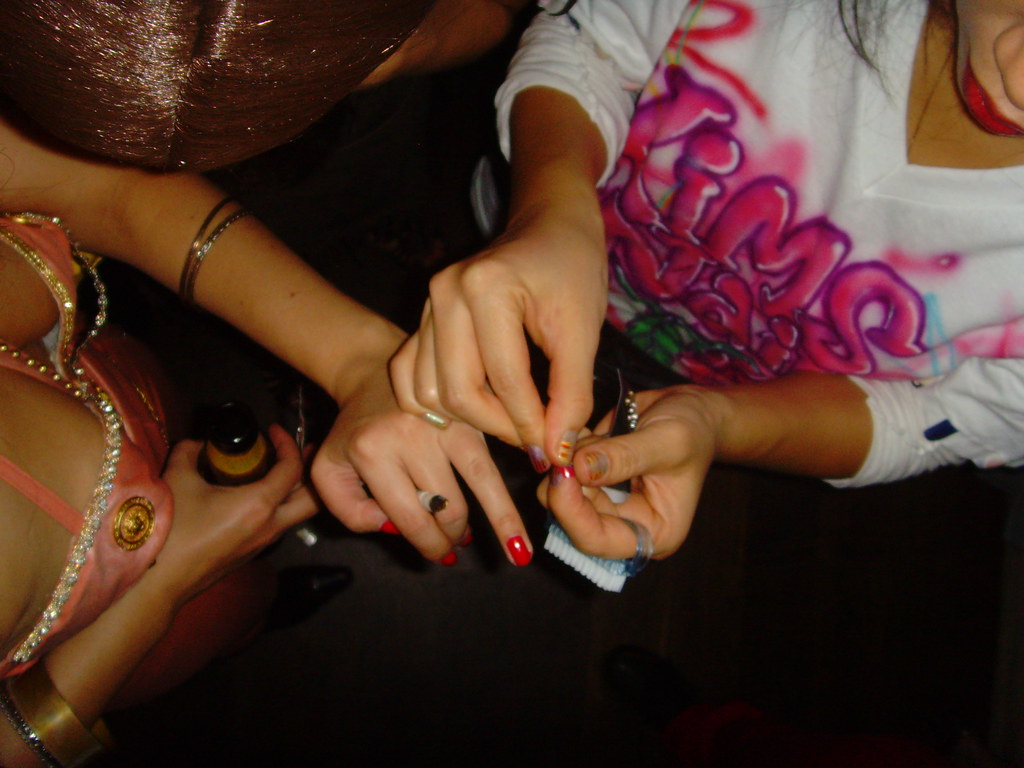 Depiction of one bedazzling another's fingernails.